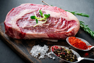 Fototapeta na wymiar Fresh raw Rib eye Steak with seasonings and red pepper on cutting Board on grey background, close up