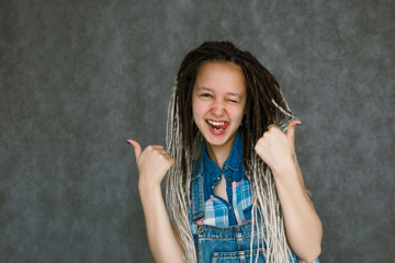 The girl in the dreadlocks is smiling. Smiling girl on gray background. Portrait of a teenager with...