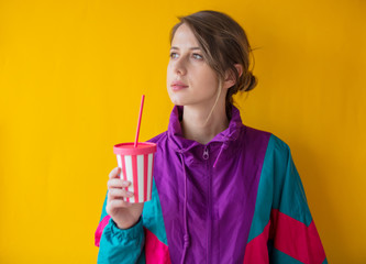 Young woman in 90s style clothes with cup on yellow background