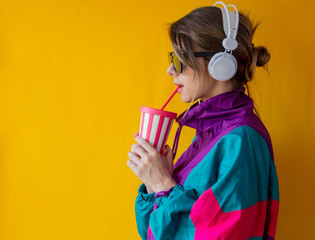 Young woman in 90s style clothes with cup and headphones