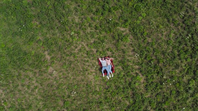Happy young couple lying on the grass in the meadow. The camera slowly flies away from them. Aerial top down. 4K.
