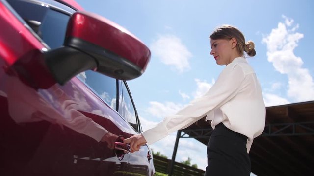 Close-up of attractive female in business clothes using modern technology to unlock car doors holding cellphone with special application. Formally dressed businesswoman opening door and getting in car