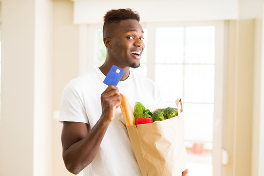 African american man holding paper bag full of groceries and holding credit card as payment