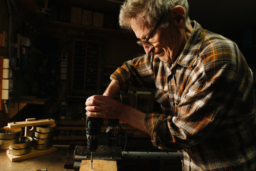 Amateur senior carpenter at his workbench, using hand drill