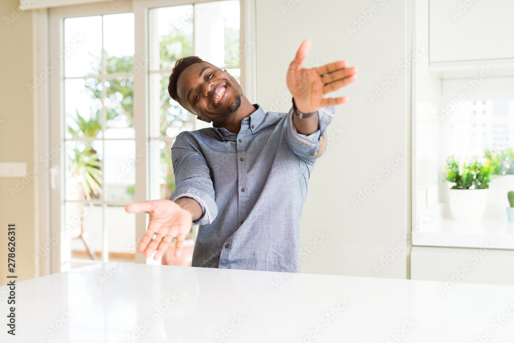 Canvas Prints Handsome african american man on white table looking at the camera smiling with open arms for hug. Cheerful expression embracing happiness.