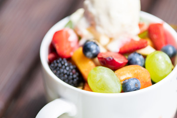 Close up of bowl with healthy fresh fruit salad with ice cream on wooden background.