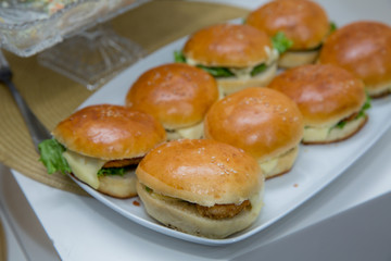 Beautifully decorated catering banquet table with different hamburgers burgers sandwiches on a plate on corporate birthday . Mini or Small Burger Canape in Luxury Restaurant for Brunch Time .