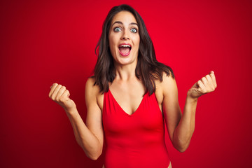 Beautiful woman wearing bikini swimwear over red isolated background celebrating surprised and amazed for success with arms raised and open eyes. Winner concept.