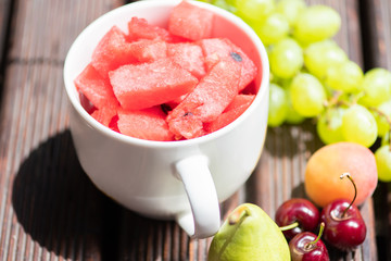 Bowl with delicious watermelon salad on wooden table with arranged fruit around.
