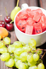 Bowl with delicious watermelon salad on wooden table with arranged fruit around.
