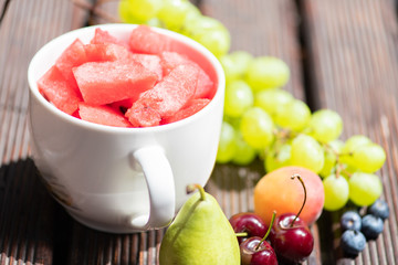 Bowl with delicious watermelon salad on wooden table with arranged fruit around.