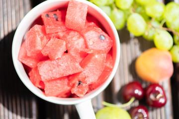 Bowl with delicious watermelon salad on wooden table with arranged fruit around. Top view.