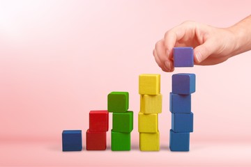 Obraz premium Hand with toy wooden blocks stack, towers of blank multicolor box cubes over white background