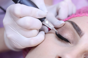 Young woman having permanent makeup on eyes in beautician salon