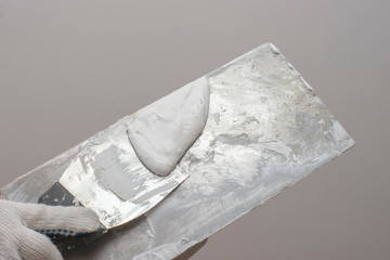 A hand with a small spatula smears the putty on a large spatula. Against the background of white...