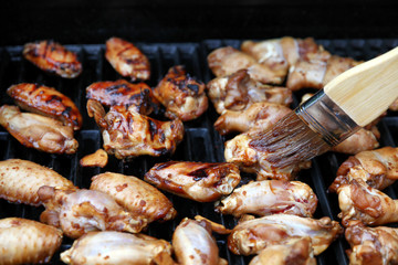 Close up of an open barbecue grill cooking chicken wings while being brushed with sauce