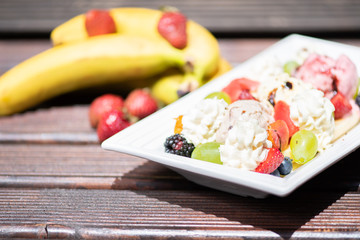 Plate of healthy fresh fruit salad with ice cream on the wooden background.