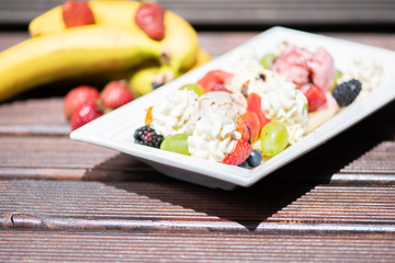 Plate of healthy fresh fruit salad with ice cream on the wooden background.