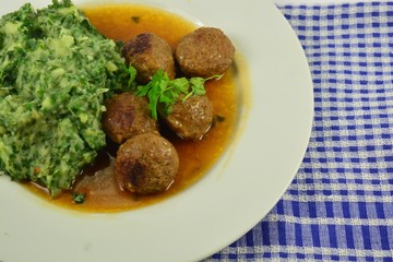 meatballs with kale potatoes and sauce on a white plate with white and blue tea  towel