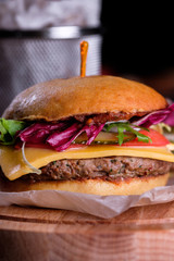 Gluten Free closeup homemade tasty burger on wooden board with organic beef, tomato, cheese and red onion. Delicious baked potatoes in bowl.
