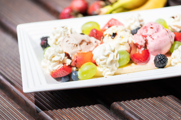 Plate of healthy fresh fruit salad with ice cream on the wooden background.