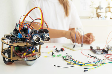A cute girl constructs metal robot and program it. The boards and microcontrollers are on the...