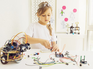 A cute girl constructs metal robot and program it. The boards and microcontrollers are on the table. STEM education inscription. Programming. Mathematics. The science. Technologie. DIY. 