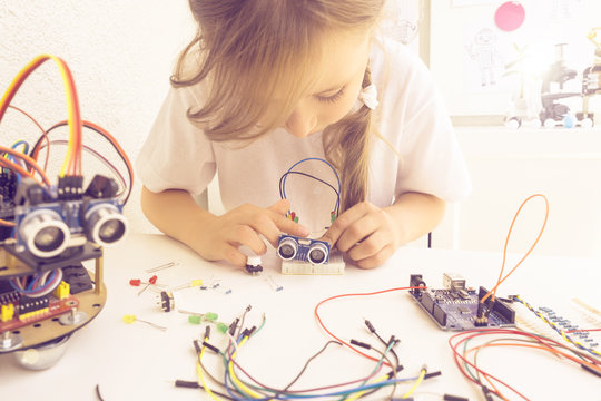 A cute girl constructs metal robot and program it. The boards and microcontrollers are on the table. STEM education inscription. Programming. Mathematics. The science. Technologie. DIY.  - Powered by Adobe