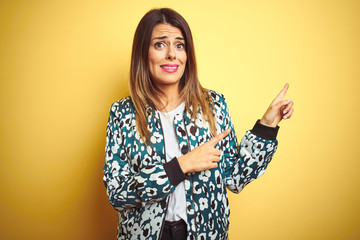 Young beautiful woman wearing casual jacket over yellow isolated background Pointing aside worried and nervous with both hands, concerned and surprised expression