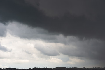 A stormy dark sky with white in the bottom, gray in the middle and black clouds on the top of the frame and a cityscape