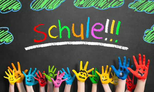 viele angemalte Kinderhände mit Smileys vor Kreidetafel mit dem Wort "Schule" 
