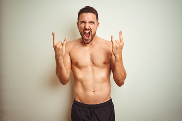 Young handsome shirtless man over isolated background shouting with crazy expression doing rock symbol with hands up. Music star. Heavy concept.