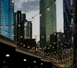 A hanging string of lights at Queen Victoria Markets with the skyline of Melbourne city in the...