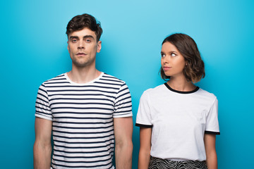 Fototapeta premium positive young girl looking at offended boyfriend on blue background