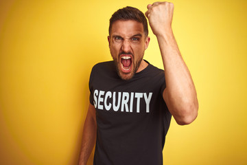 Fototapeta premium Young safeguard man wearing security uniform over yellow isolated background angry and mad raising fist frustrated and furious while shouting with anger. Rage and aggressive concept.