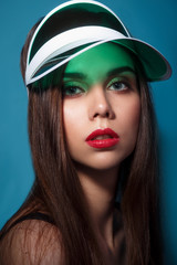 Beautiful woman with make-up and red lips in green gel cap visor on the blue background