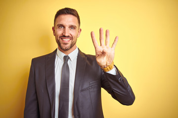 Young handsome business man over yellow isolated background showing and pointing up with fingers number four while smiling confident and happy.