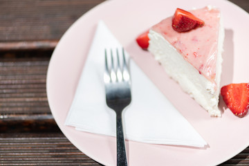 Slice of fresh strawberry tart on the pink plate with layered cream.