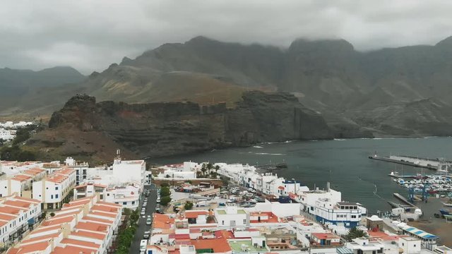 Aerial view of Agaete, Gran Canaria, Canary Islands. Port in a small bay with expensive yachts, white houses and a promenade. The mountains Parque Natural Tamadaba