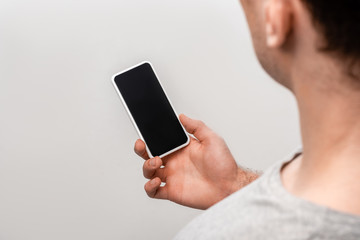 cropped view of man holding smartphone with blank screen isolated on grey