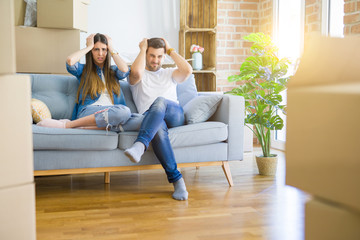 Young beautiful couple relaxing sitting on the sofa around boxes from moving to new house suffering from headache desperate and stressed because pain and migraine. Hands on head.