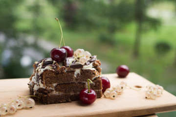 Chocolate cake with cherry on a beautiful bokeh background, with berries and flowers on a summer picnic