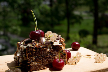 Chocolate cake with cherry on a beautiful bokeh background, with berries and flowers on a summer picnic