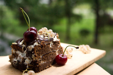 Chocolate cake with cherry on a beautiful bokeh background, with berries and flowers on a summer picnic