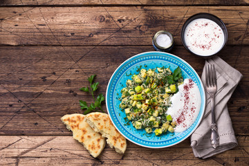 Traditional Turkish fried eggs with zucchini and herbs with yoghurt garlic sauce and fresh tortillas on a wooden table, top view. delicious healthy breakfast