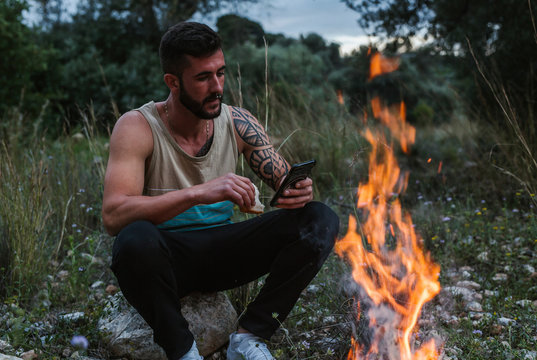Man sitting at campfire in rural landscape using cell phone