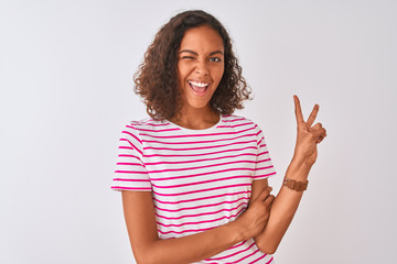 Young brazilian woman wearing pink striped t-shirt standing over isolated white background smiling with happy face winking at the camera doing victory sign. Number two.