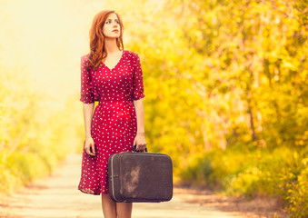 Redhead girl with suitcase at tree's alley.