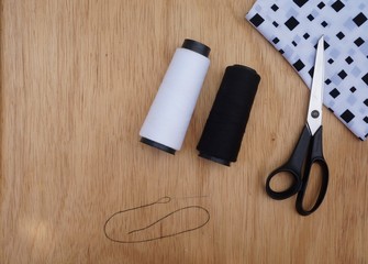Sewing tools including fabric, scissors, needles and threads on a wooden background with empty place for text.