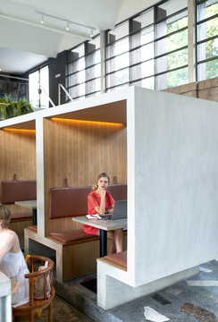Lifestyle shot of trendy cafe with pretty blonde caucasian millennial female using laptop computer and notepad at large wooden table